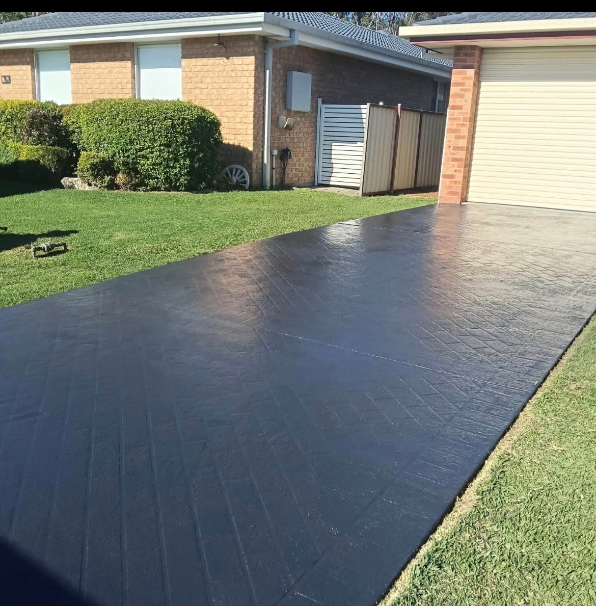 Freshly painted black stamped concrete driveway — residential property finished result